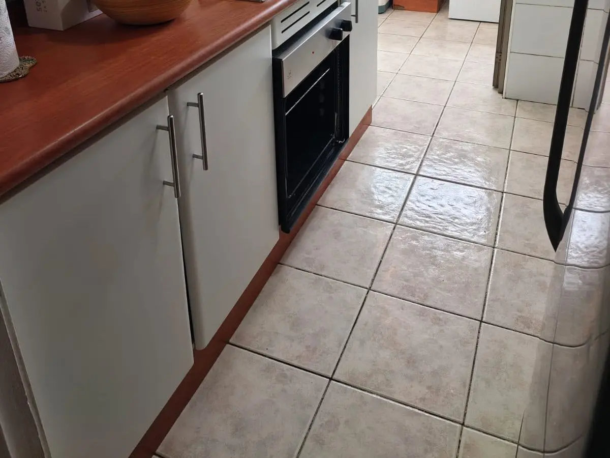 Cocina de un depto con muebles blancos, el horno empotrado y el piso de cerámica brillante después del aseo