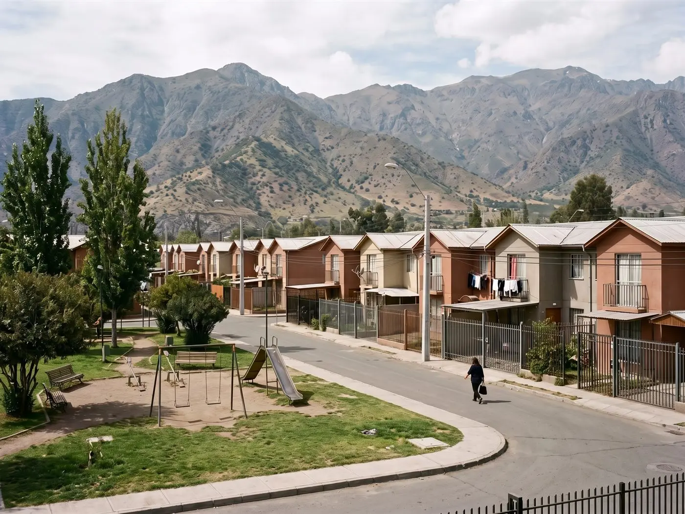 Casas pareadas de dos pisos y plaza con juegos en una villa de Puente Alto, precordillera al fondo