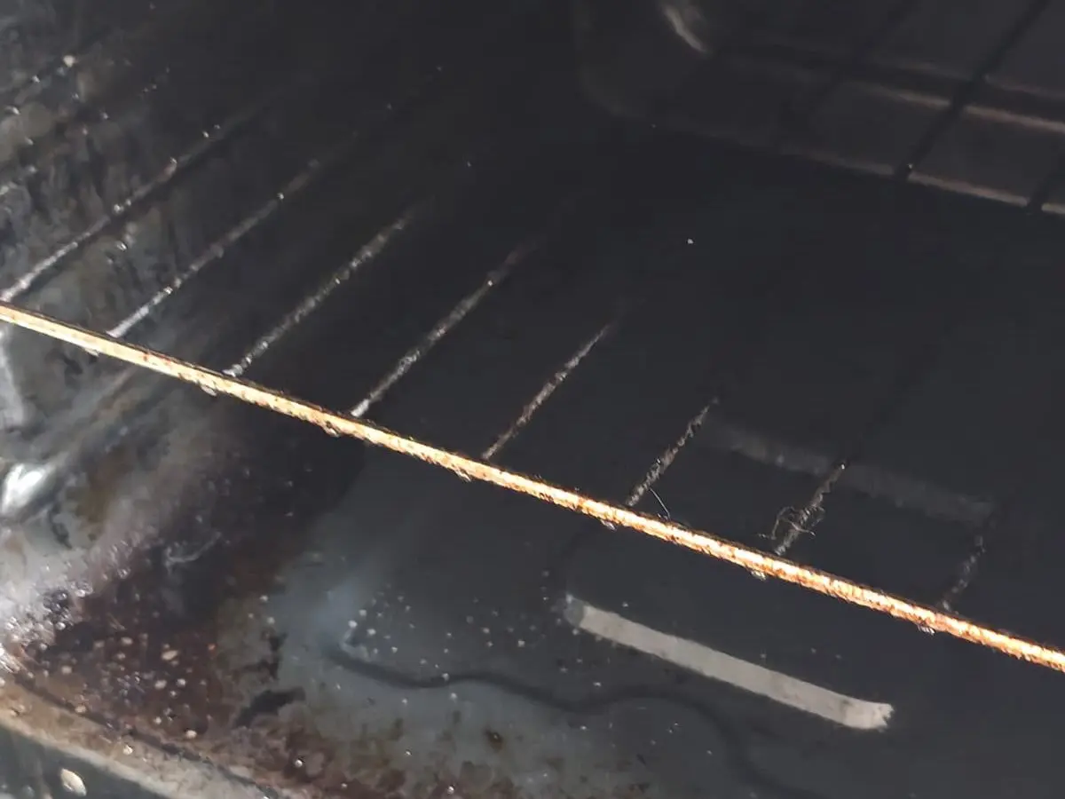 Interior de un horno con grasa quemada y restos pegados en la base y la parrilla, antes del aseo