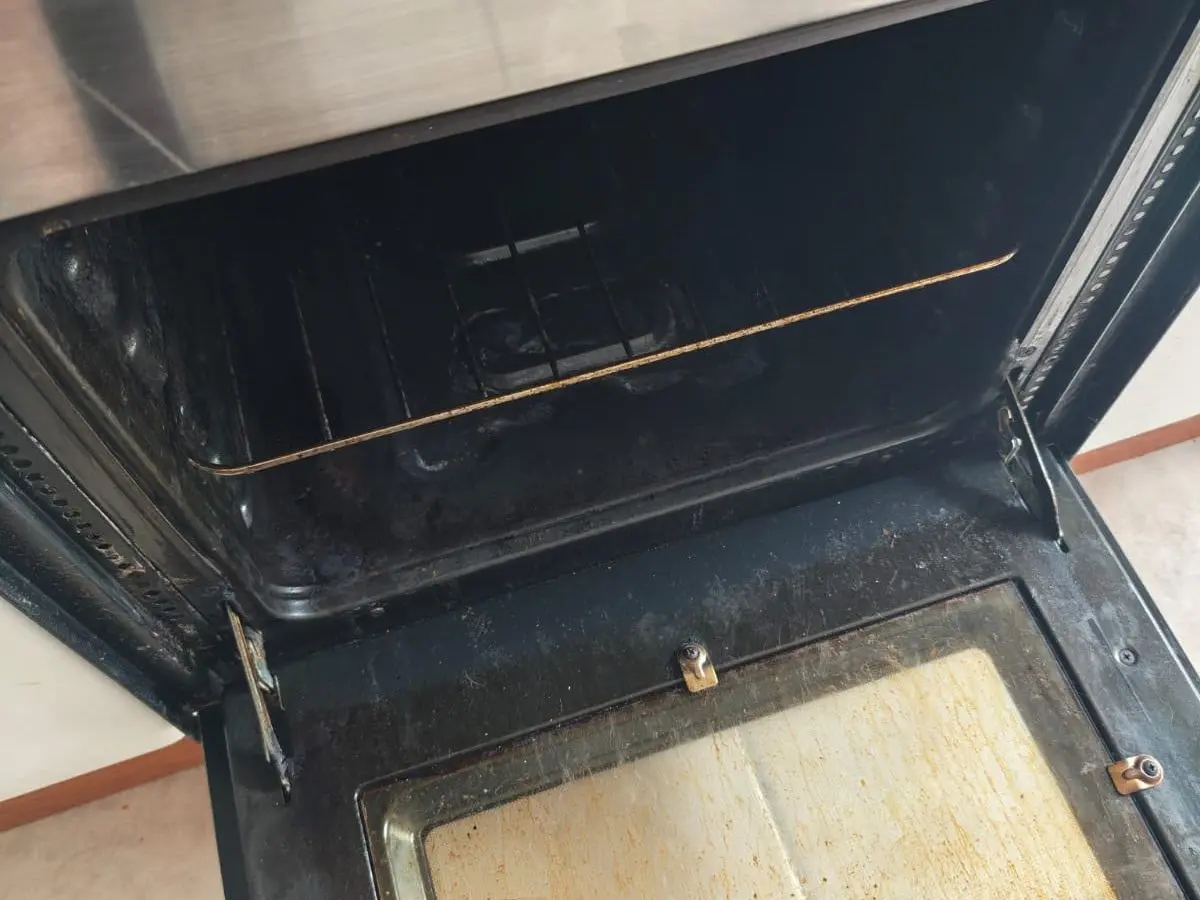 Puerta de un horno abierta, con el vidrio interior manchado de grasa, antes del aseo